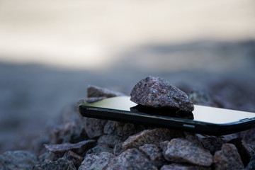 Cell phone with broken glass on gravel granite stones, unbreakable gadget