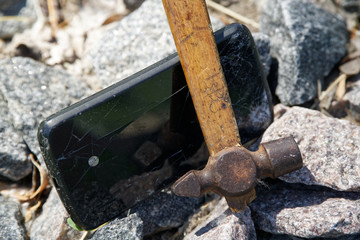 Smartphone broken glass with hammer on gravel stones. Selective focus