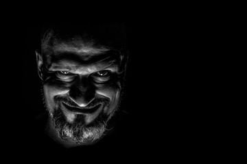  Face with a bearded man grimace against a dark background with sharp shadows. Comedic, fabulous villain or negative character conception with copy space. - obrazy, fototapety, plakaty