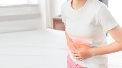 Asian woman unhappy lying on the bed looking sick, suffers from stomach ache in the bedroom, stomachache because of menstruation and eating spoiled food, Chronic gastritis. Abdomen bloating concept