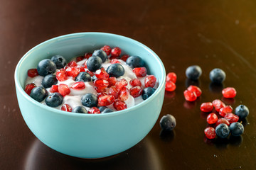 Additional blueberries and pomegranate on a bowl of flavored probiotic yogurt being served for breakfast on an old wooden table