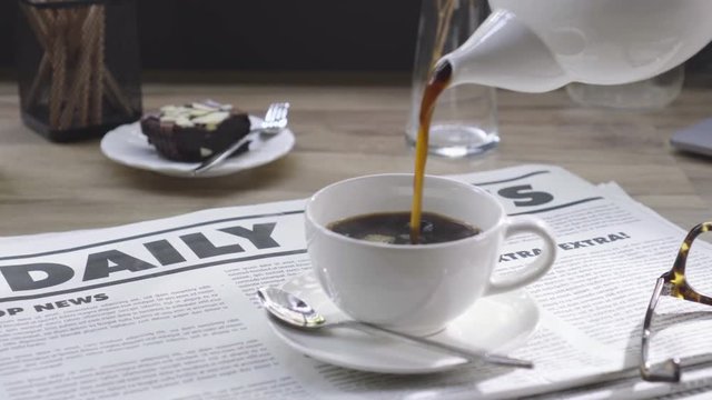 Hand holding and pouring hot coffee Into white cup on newspaper with view of room on the morning, Daily Newspaper mock-up concept