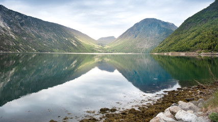 Evening landscape of Norway fjord in calm with reflection of mountains and sky in calm water