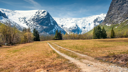 Fototapeta premium dirt road in an intermountain valley among snow covered mountain peaks in spring in Norway
