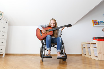Disabled young woman in wheelchair playing the guitar. Wide angle, full body.
