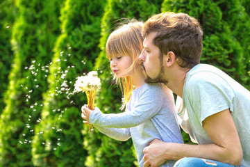 Father and daughter blowing dandelion on summer garden. Happy family.