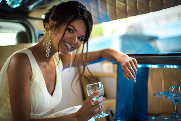 Young attractive woman in a limousine holding a glass. She's wearing a white dress. Wedding or...