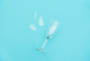 Broken champagne glass with splinters on blue background with copy space. Concept fight against...