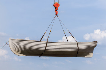Rowing boat hanging on a crane hook on a blue sky background