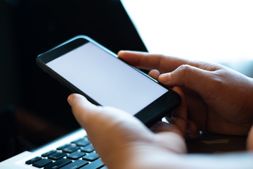 hand using a mobile phone with white blank screen over the laptop