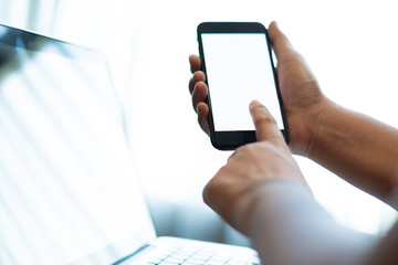 hand using a mobile phone with white blank screen over the laptop