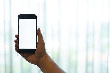 hand using a mobile phone with white blank screen against white curtain background