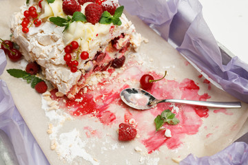 Delicate meringue pie with cherries, red currants and raspberries with mint leaves and spoon are on a tray