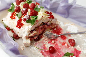 Partially eaten insanely delicious meringue cake with ripe fruit and a spoon lie on a tray