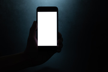 silhouette hand holding a mobile phone with blank wihte screen in the dark darkness against dark blue background