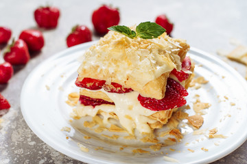 Slice Confectionery Napoleon Cake with Strawberry. Portion of Custard Cream Dessert with Red Ripe Berry and Decorated Green Leaves on Top. Crumbs Around White Plate. Bakery Tasty Sweet Dish Closeup
