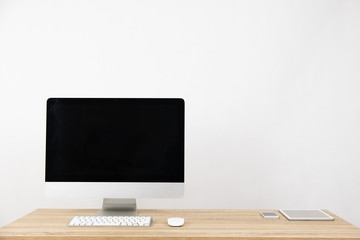 Modern PC Monitor and blank screen, mouse, keyboard and some stuff on the wooden table. White background and copy space. Business or Work space theme