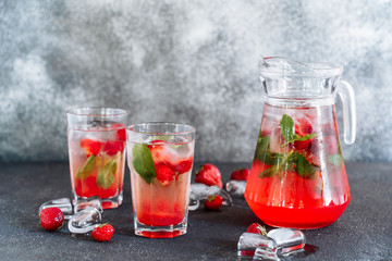 Glasses and Carafe with Fresh Strawberry Drink. Cold Refreshing Beverage Mixed with Herbal Mint Cocktail in Cup. Ice Cube and Ripe Berry Around of Flask. Summer Juicy Vitamin Water Side View