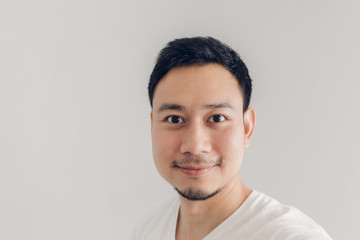 Naklejka premium Uśmiechnięty mężczyzna bierze selfie z białą koszulką i szarym tłem.
