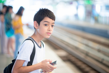 Little student boy waiting for train on platform with mobile in hands