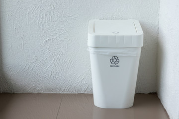 white plastic trash bin on floor of living room. indoor recycle bin at conner.