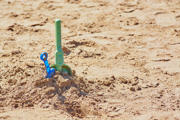 Fototapeta na wymiar Baby shovels stuck in sand on sandy shore of beach.