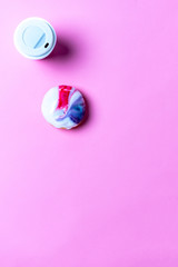 Top-down-view of a coffee and a doughnut on a bright pink background