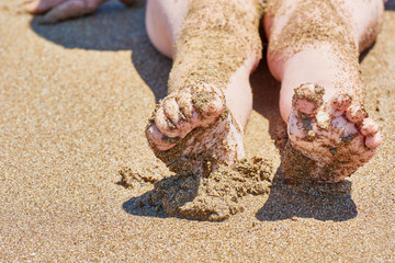 Stretched baby feet in sand on sea beach on sunny day.