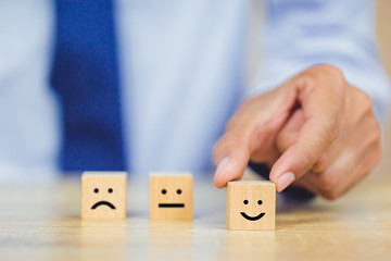 customer pressing smiley face emoticon on wood cube, Service rating, satisfaction concept.