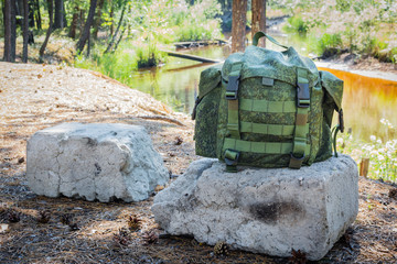 Small backpack for hiking lies on concrete ruins in forest against backdrop of river in summer.