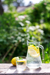 fresh lemonade, glass and one lemon on wooden old table against a green grass background