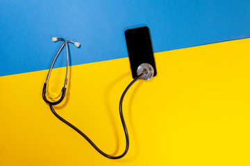 A stethoscope connected to a phone laying on a yellow and blue surface