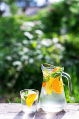 fresh lemonade with orange and a glass on wooden old table against a backdrop of green grass