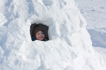 Happy cheerful boy sitting in an igloo in winter