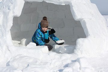Happy cheerful boy building an igloo in winter