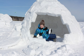 Happy cheerful boy with a piece of snow in his hands sitting an igloo in winter