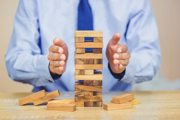 Hand of businessman pulling out or placing wood block on the tower, plan and strategy in business.