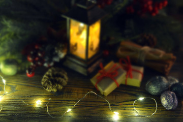 Shining garland with lights in focus and old lantern with gifts and decorations in blur.