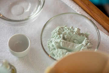From above cups and loose powder in glass bowl on fluffy white towel