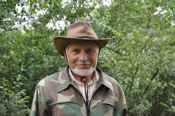 Middle aged traveler. Portrait of a handsome adult man with a gray beard and hat in camouflage clothing.