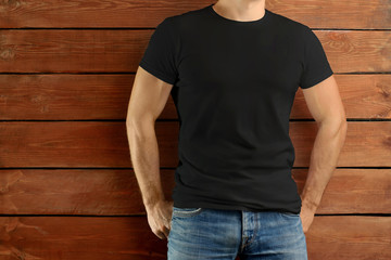 Athletic fit guy in a black T-shirt and blue jeans standing on a brown wooden studio background.