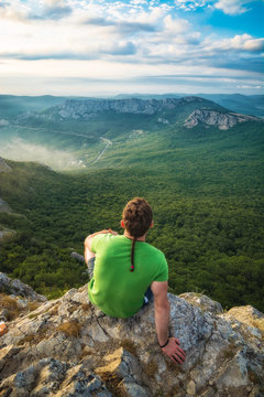 Young man hiker sitting on a cliff edge