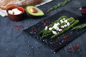 Served frilled asparagus with Cheese Feta and spices on stone on dark background. Healthy food concept. Diting. Gluten free, vegan. Copy space. Flat lay food