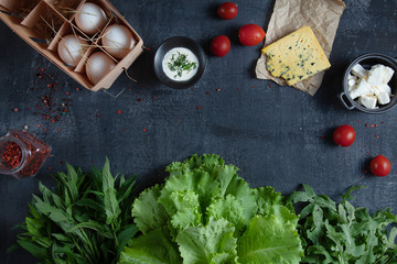 Ingridients for cooking salad. Fresh, organic vegetables, eco eggs and greens. tomato and cheeses on dark stone background with copy space. Flat lay. Healthy food concept