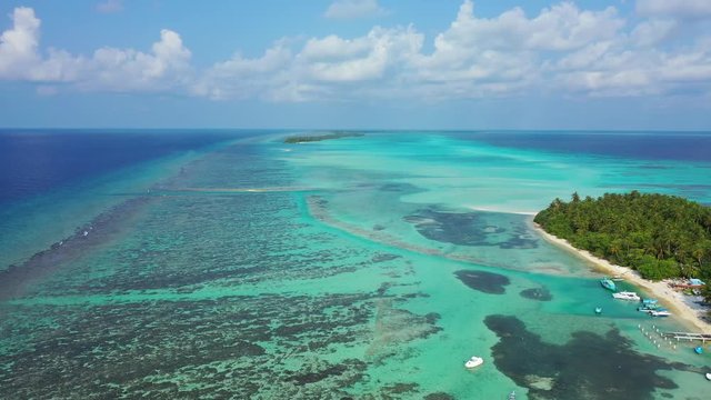 Aerial view of a tropical island with a forest and village and radio mast on it. In the turquoise sea in Bali. Next to a reef. Truck right and pedestal up. Sideways movement.