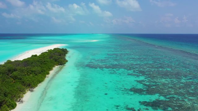 Aerial view along a tropical island on the left, with a palm tree in it. In turquoise water in Bali. Truck right with a pan left.