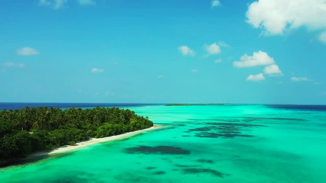 Aerial view of the turquoise green sea under a blue sky with some clouds. A tropical island on the left. Pedestal up, dolly in