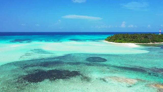 Aerial view of a tropical island. In the turquoise and blue sea in Hawaii with patterns of reefs. Palm trees and a village on it. Dolly out, pedestal up