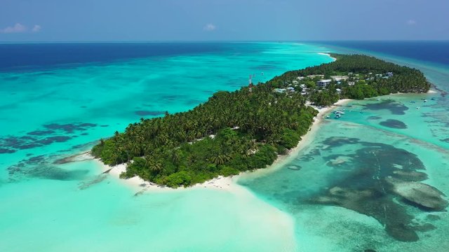 Aerial view of a the turquoise sea in Thailand, a tropical island with a village on it. Reefs in the water. Dolly out