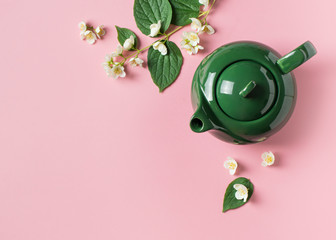 Jasmine tea with teapot, flowers and leaves on pink background